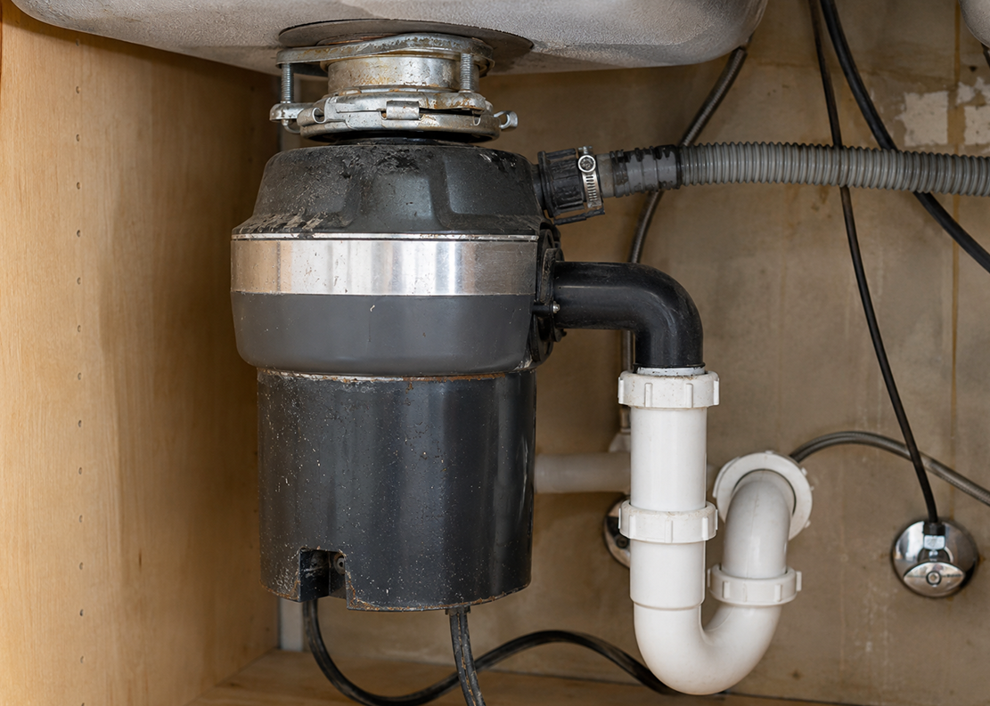 Worn garbage disposal under sink with plumbing connections